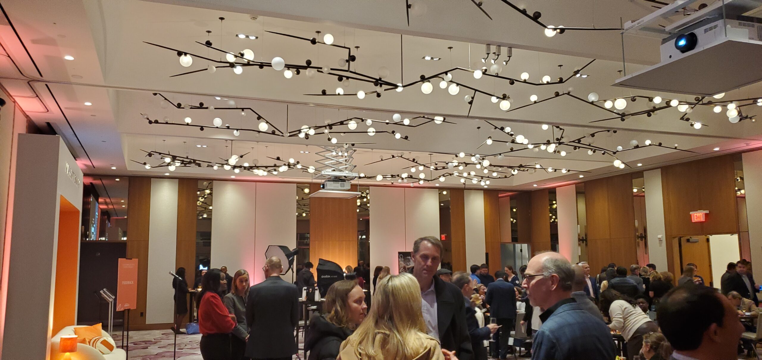 Attendees networking under modern architectural branch chandeliers in the grand ballroom