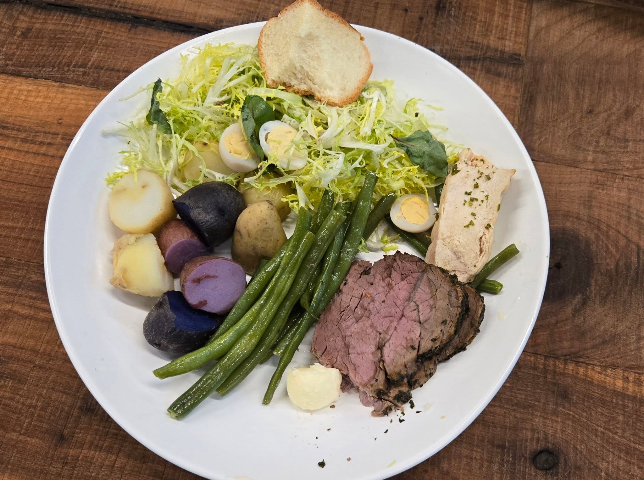 Gourmet plated luncheon featuring tender beef filet, quail egg, roasted fingerlings, and haricots verts