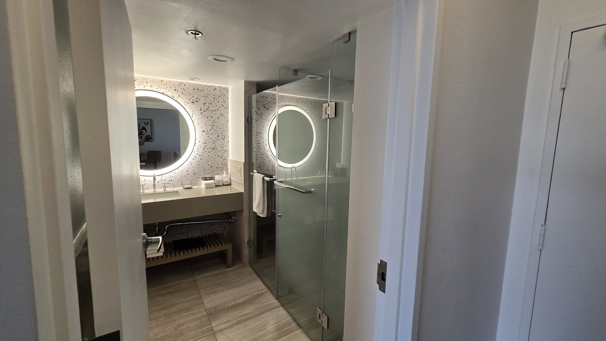 Circular backlit LED halo mirror mounted against black-and-white terrazzo wall
